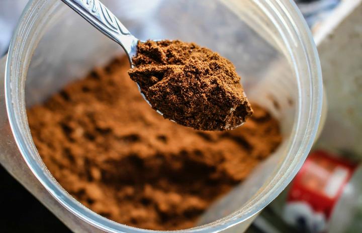 A chocolate protein powder scoop in spoon with protein shaker bottle