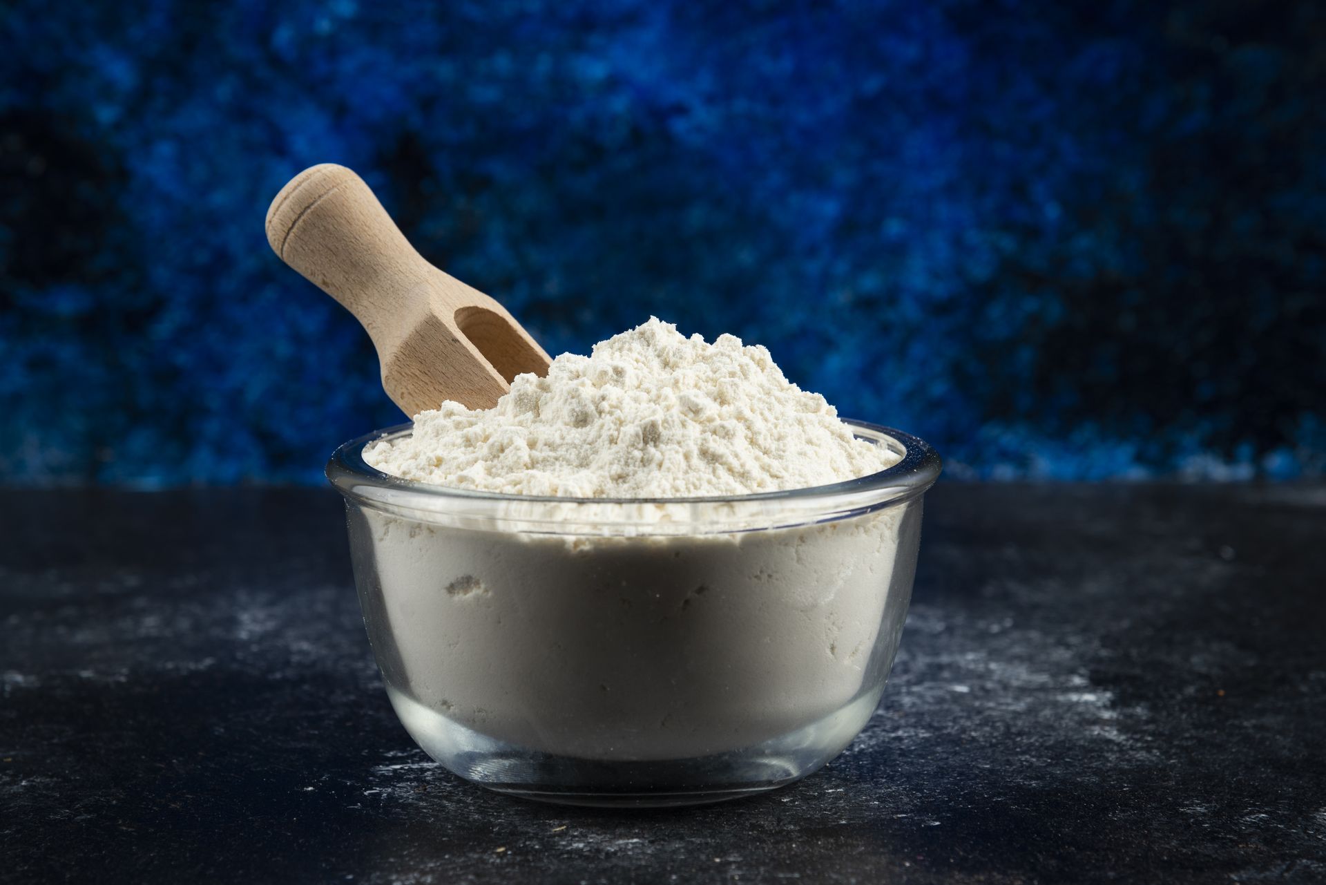 A bowl of flour with yeast and scooper in a blue background