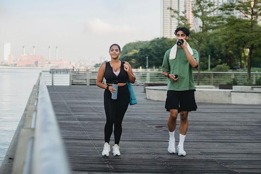 Un hombre y una mujer caminando en el parque junto al mar después de hacer ejercicio