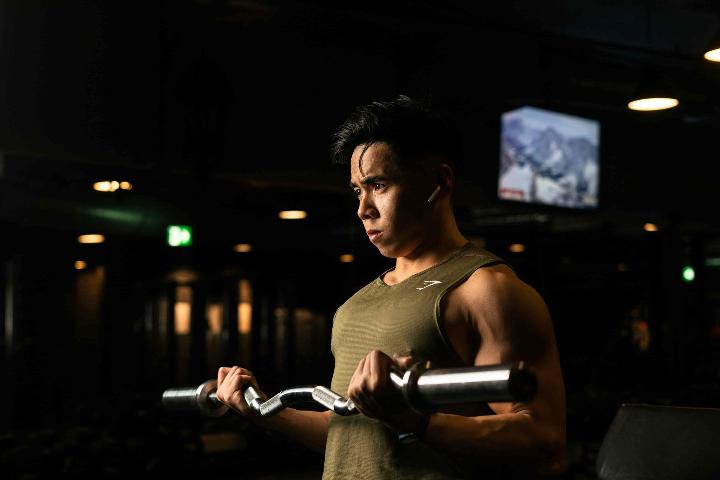 Un hombre haciendo entrenamiento con pesas llevando tubos de acero dentro del gimnasio oscuro