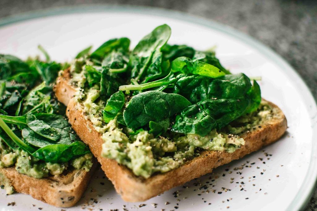 Espinafre em cima do pão torrado com pasta de pesto num prato