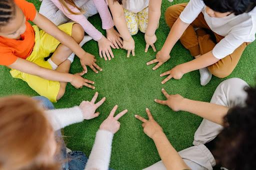 Children are sitting with two fingers lay down in the grass floor