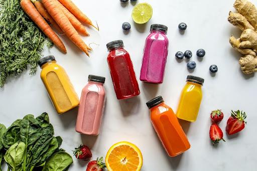 Une image de jus détox de différentes couleurs avec du gingembre, des carottes, des fraises et des mûres